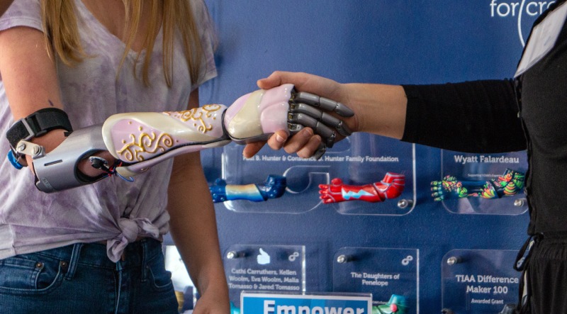 Una niña biónica sin límites estrecha la mano a la estudiante universitaria de UCF SVAD que pintó su manga biónica.